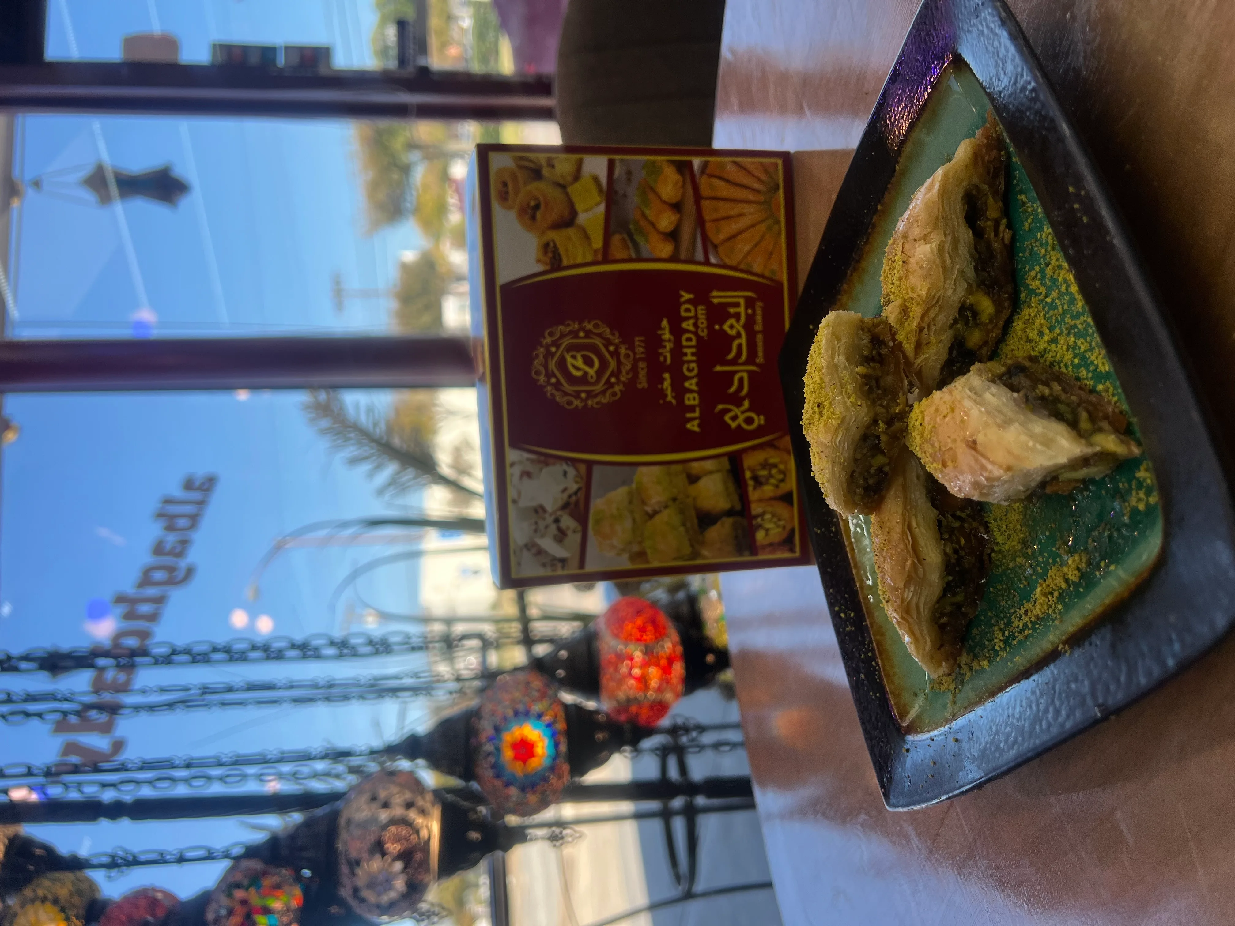 A boxed Al-Baghdady bakery selection next to a plate of fresh pistachio baklava