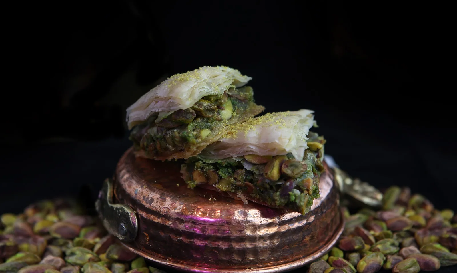 Pistachio baklava layered on a hammered copper dish, surrounded by raw pistachios
