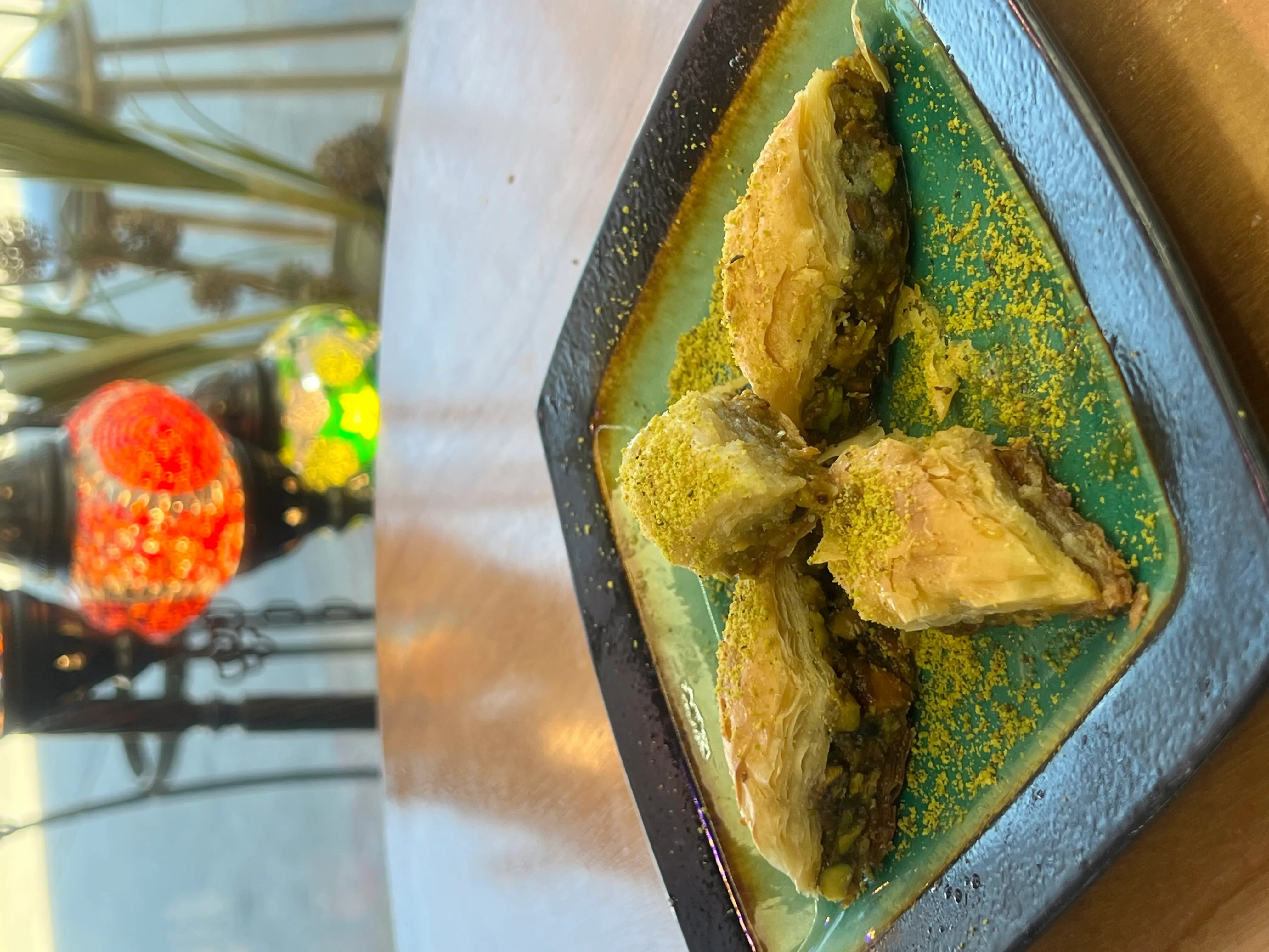 Pistachio baklava plated on a green ceramic dish beside Turkish mosaic lamps