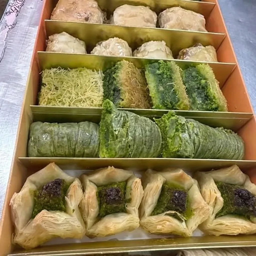 An Al-Baghdady catering box with compartments of mixed baklava, pistachio rolls and Iraqi sweets