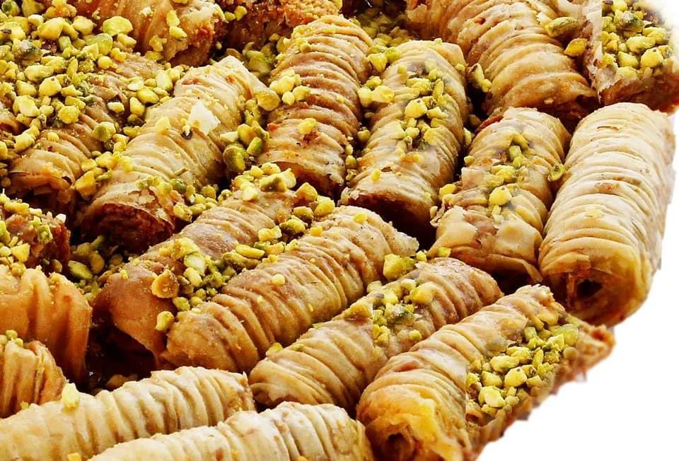 Crisp phyllo ladyfinger rolls dusted with pistachio on a ridged glass plate