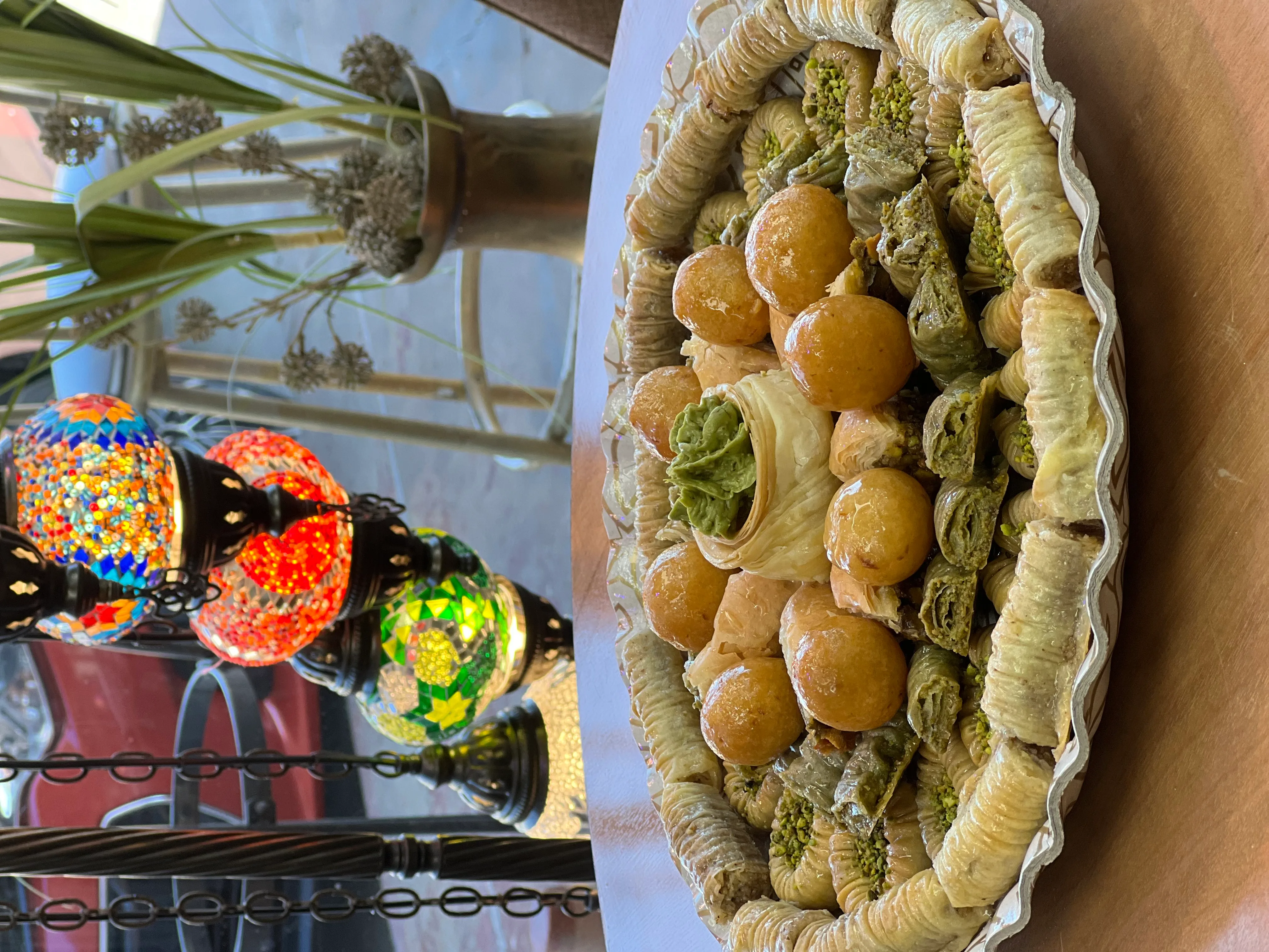 A large oval platter of mixed Iraqi baklava and bird's nest pastries in the bakery window