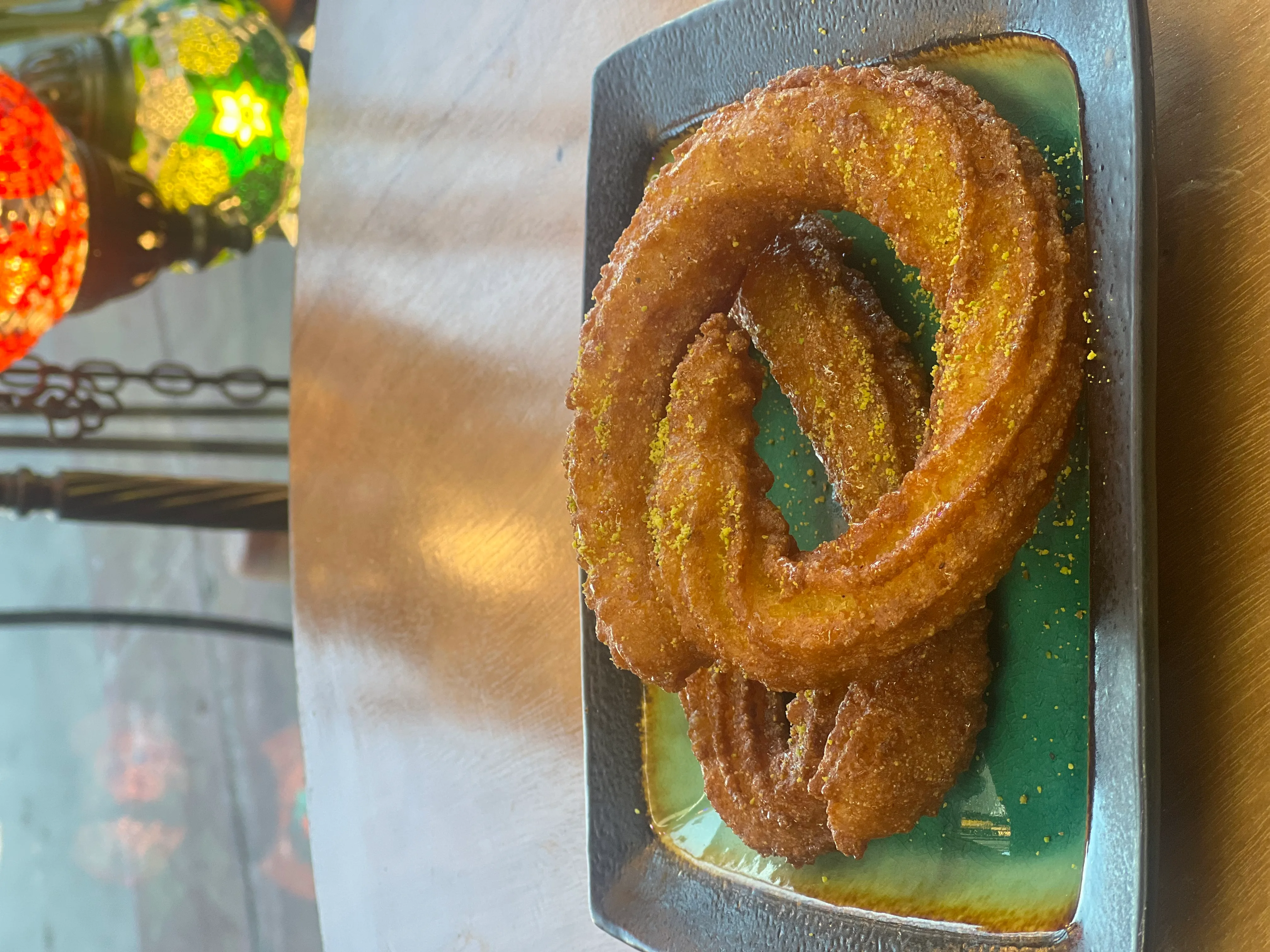 Two golden zalabia rings, crisp and syrup-soaked, plated on green ceramic